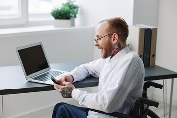 Fototapeta na wymiar A man wheelchair, businessman in the office working laptop, working online, social networks startup, integration into society, the concept of working a person with disabilities, a real person close-up