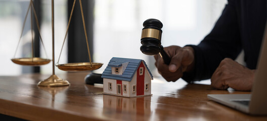 Close-up of a house in front of a lawyer holding a hammer and a laptop silver brass scales on a wooden table in his office, law, legal services, advice, justice and real estate ideas.