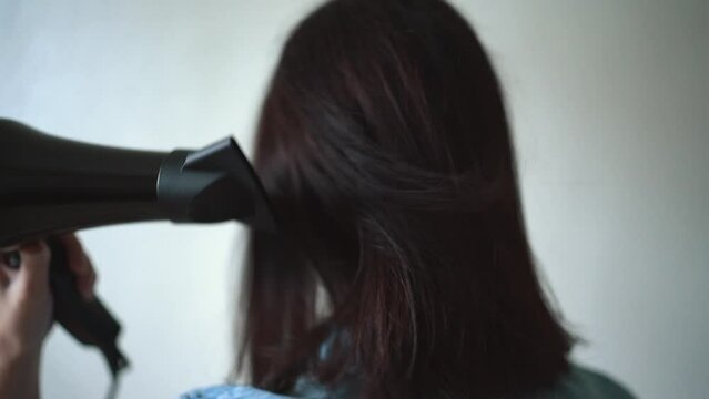 The girl dries her hair with a hairdryer. Concept of well-groomed and beautiful woman. Close up video of Woman drying hair using black hair dryer.	