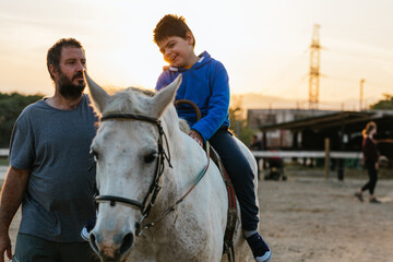 Physiotherapist working with a child with a disability in an equine therapy session. - obrazy, fototapety, plakaty