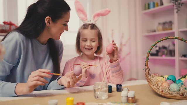 Little girl and her mom painting Easter eggs together, having fun, childhood