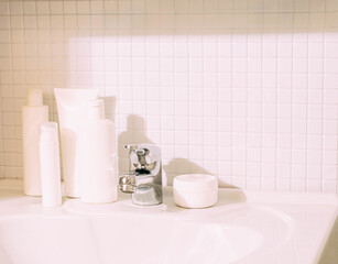 White bottles with various cosmetics stand on sink in bathroom. Cleanliness and order in the house