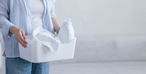 Woman holds basket with dirty laundry bottle of detergent in her hands. Cleaning wash cleanliness