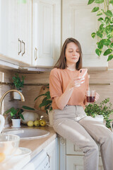 woman is sitting on table in kitchen chatting in a smartphone and drinking coffee in the morning for breakfast, brewing pourover. cappuccino americano. eating drinking for lunch, happy woman enjoys.