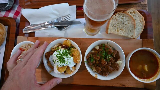 Budapest, Hungary, August 2022. Top view footage of an appetizing tasting tray of local delicacies, starting with goulash on the right and going to the left with other dishes with vegetables.