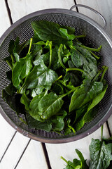 Washed fresh mini spinach in a colander on the old wooden table