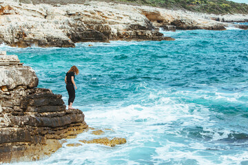 young slim woman standing on the cliff edge looking at sea
