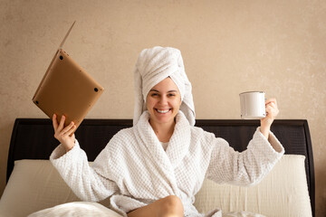 smiling woman working at home in a white terry dressing gown with a towel on her head