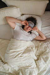 A smiling woman wakes up in her bed in white sheets