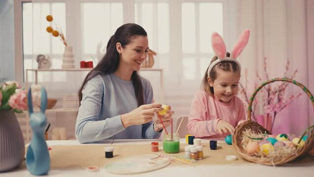 Little girl and mother playing while decorating Easter eggs, family traditions