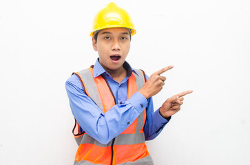 asian construction worker wearing yellow safety helmet and vest smiling and pointing finger with happy and shocked expression. billboard model advertisment concept. 