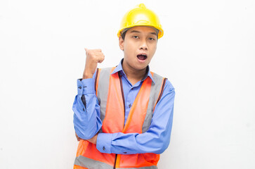 asian construction worker wearing yellow safety helmet and vest smiling and pointing finger with happy and shocked expression. billboard model advertisment concept. 