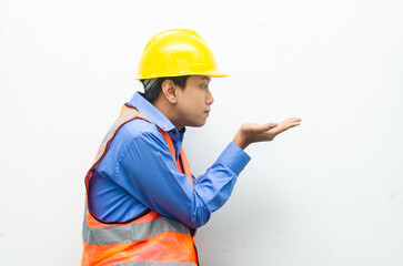 asian construction worker wearing yellow safety helmet and vest smiling and pointing finger with happy and shocked expression. billboard model advertisment concept. 