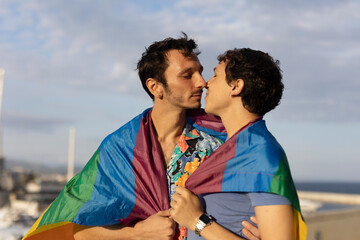 Happy young couple with rainbow flag. Two men kissing outside.