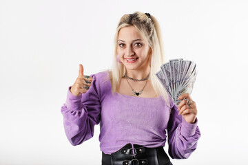 Cute millennial woman standing isolated over white background holding bunch of money and making okay gesture and looking to the camera with smiles. Win money prize lottery showing thumb-up.