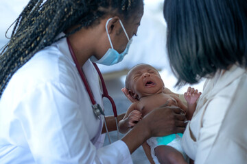 African Doctor checking sick newborn baby, baby unhappy and crying, Mom looks on with concern