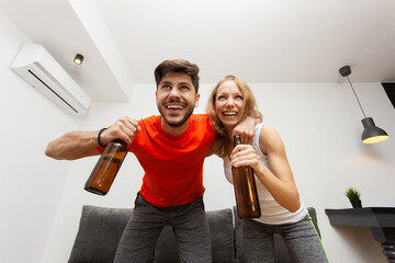 couple at home watching the game on tv having beer cheering and yelling