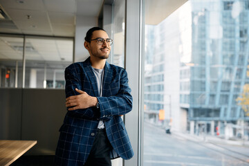 Smiling Hispanic businessman looking through window of his office.