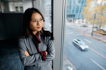 Pensive Asian businesswoman looking through window in office.