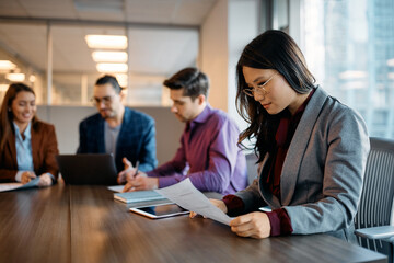 Asian businesswoman reads documents during meeting with coworkers in office.