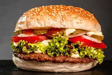 Hamburger with onions tomatoes cucumber and lettuce against dark gray background.Hamburger with onions tomatoes cucumber and lettuce against dark gray background.