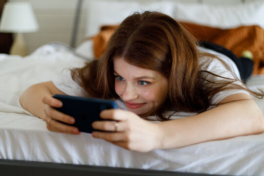A young girl watches a series on a smartphone in bed, leisure. Close-up, portrait in home interior.