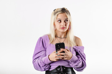 Fototapeta premium Portrait of young blonde woman isolated over white background smiles, looks at the empty copy space while holding the phone at chest level. Looking an advertisement or a campaign or a discount.