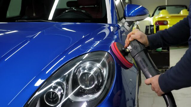 A man polishes a blue car with a car polishing machine at a car dealership. Car detailing and polishing concept.