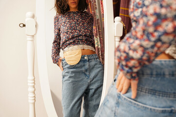 young woman looking at abdomen with an ostomy bag in the mirror. Resilience in colon cancer