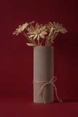 The flowers is made of straw on a red background in a cardboard vase
