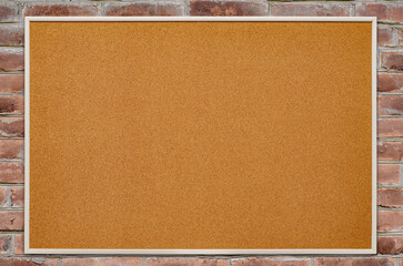An empty cork board is hanging on a brick wall. Copy space.