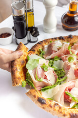 man's hand holding a slice of mediterranean pizza