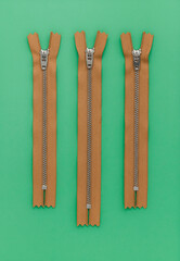 Three yellow zippers on a green background. Sewing tools. Top view. Copy space.