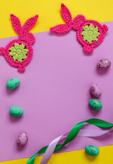 Festive greeting card with crochet Easter bunnies and colorful Easter eggs on a pink backgrond. Top view. Copy space.