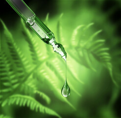 Cosmetic pipette with drop on a green blurred natural background with bokeh