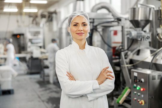 Portrait of a successful food factory manager in sterile uniform with arms crossed smiling at the camera.