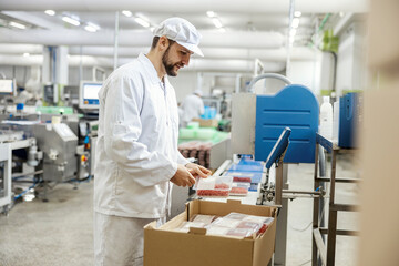 A meat processing plant worker is packing ground meat into the boxes while standing next to a...