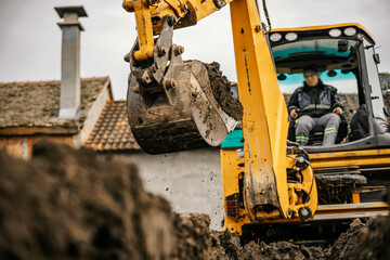 Fototapeta premium A worker in a backhoe is digging pit on a reconstruction area.