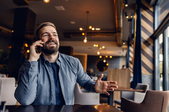 A happy man is sitting in cafeteria and talking on the phone.