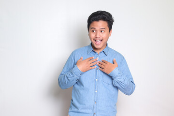 Portrait of excited Asian man in blue shirt spreading his hands sideways and holding two things, demonstrate products, welcoming someone. Isolated image on white background