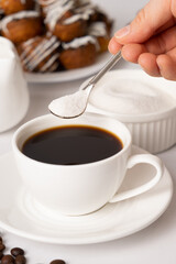 The process of pouring white sugar from a spoon into a white cup of coffee. Sugar addict, diabetes.