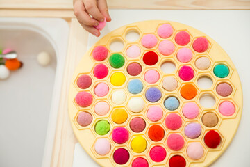 3-year-old is playing with a Russian Dumpling Maker, inserting pompoms into holes. Colored yarn balls in a plastic bag. Montessori concept. Early education, color play, fine motor skills.
