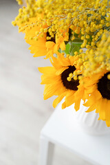 Blossom of Mimosa and sunflowers in white ceramic vase on white brick wall background with space for text