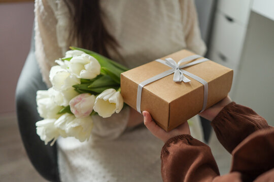 The child's hands hold a beautiful gift box with a ribbon and white tulips. Top view, close-up. Happy mother's day