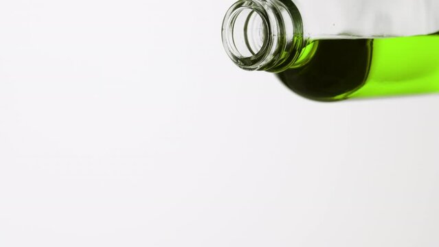 Macro shot of reagent bottle is being tilted and green oil pours from it on grey background | Abstract anti-aging cosmetics ingredients formulating concept