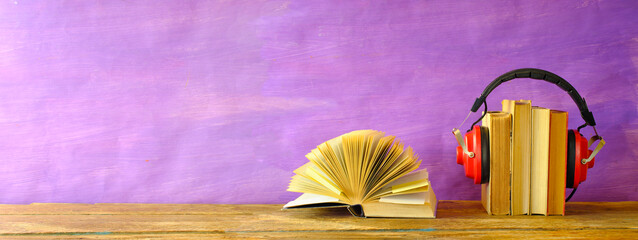 audio book concept with row of books, one opened and vintage headphones,panoramic, free copy space