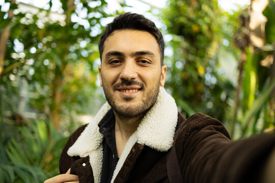 Young white man taking selfie with mobile phone in forest.