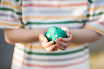 Fototapeta na wymiar Close up of two dyed eggs in childs hands. Children prepare for Easter holiday. Copy space. Selective focus.