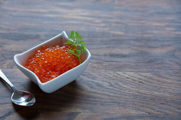 Salmon Red Caviar in ceramic bowl and spoon isolated on wooden background.