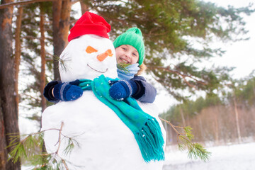 child hugging snowman in winter forest